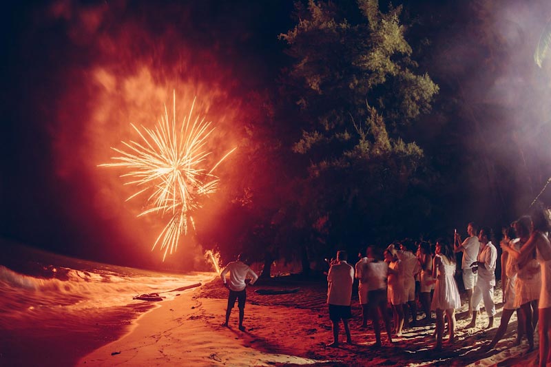 crowd standing on beach with fireworks